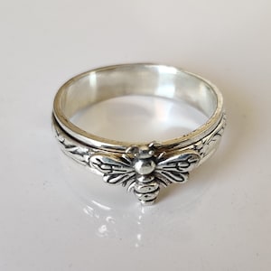 Op de afbeelding: Een zilveren draai ring met een bij ontwerp. De ring is gegraveerd met bloemmotieven.