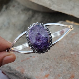 Pode incluir: Um bracelete de prata com uma incrustação oval de concha de abalone roxa e prata. A concha tem um padrão de redemoinho e está engastada em um bezel de prata.