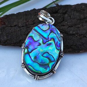 May include: A silver pendant featuring a blue, green and purple abalone shell inlay. The pendant is oval shaped and has a silver bail.