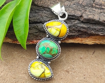 Könnte beinhalten: Silberanhänger mit drei ovalen Steinen. Die oberen und unteren Steine sind gelb und weiß, der mittlere Stein ist grün. Der Anhänger hat ein gedrehtes Seildesign um jeden Stein. Der Text "Daffodil Jewelry Co." ist sichtbar.