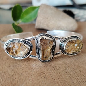 May include: Silver bangle bracelet with three faceted, light brown gemstones set in silver bezels.