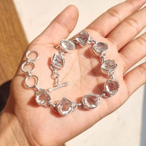 Puede incluir: Un brazalete de plata con piedras de cuarzo transparentes. El brazalete tiene un cierre de palanca.