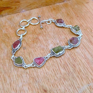 Puede incluir: Un brazalete de plata con cierre de palanca presenta seis piedras preciosas facetadas. Las piedras preciosas son una mezcla de rosa y verde, engastadas en engastes de plata.