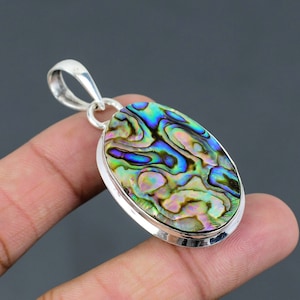Op de afbeelding: Een zilveren hanger met een ovale abalone-schelp met iriserende groene, blauwe en paarse tinten. De schelp is gezet in een zilveren bezel en heeft een zilveren bail.