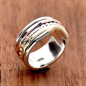 May include: A silver spinning ring with three bands of gold, copper, and silver. The ring is marked with "925" on the inside.