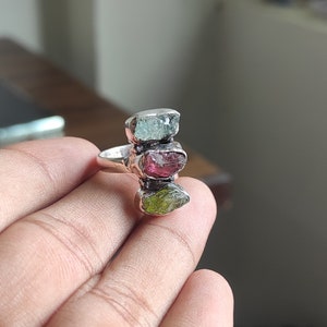 May include: A silver ring with three stacked gemstones. The top stone is light blue, the middle stone is pink, and the bottom stone is green.