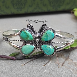 May include: A silver cuff bracelet featuring a butterfly-shaped centrepiece with four teardrop-shaped turquoise stones. The metalwork includes twisted wire detailing and small silver beads. The text Daffodil Jewelry Co is visible above the item.