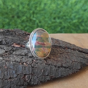 Puede incluir: Un anillo de plata con una piedra redonda, iridiscente de color verde, marrón y rojo.