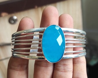 May include: A silver bangle bracelet with a large, oval-shaped turquoise gemstone set in the center. The bracelet is made of multiple thin bands of silver.