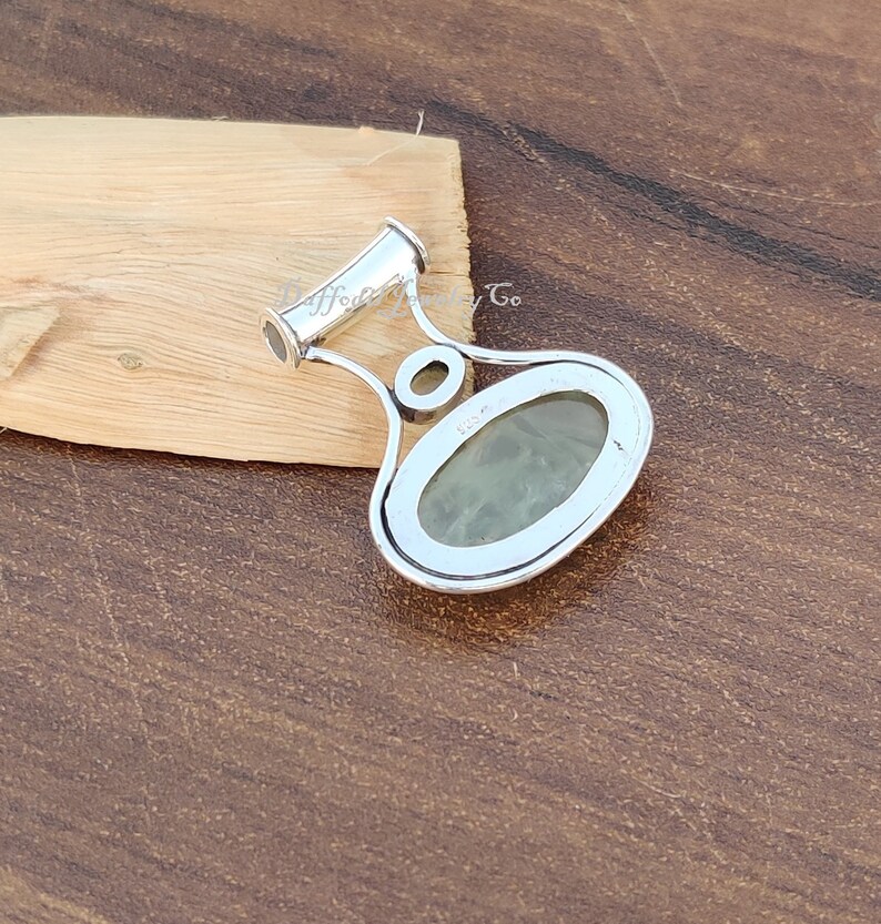 May include: Silver pendant with a green gemstone set in a silver oval frame. The pendant has a bail with a loop at the top.