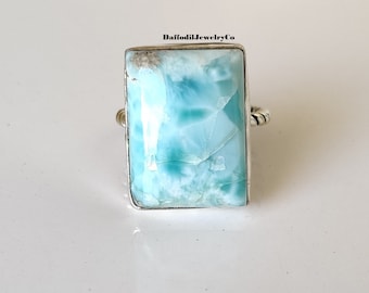 May include: A silver ring featuring a large, rectangular, light blue gemstone. The gemstone has a cloudy, marbled pattern. The ring band is twisted.