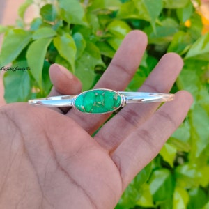 May include: A silver bangle bracelet with a green oval turquoise stone set in the centre.