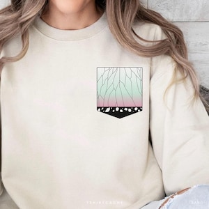 May include: Cream-colored sweatshirt with a rectangular graphic on the chest. The graphic features a geometric design with a gradient of pink and green, outlined in black, and a black bottom.