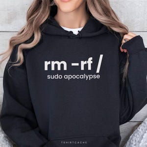 May include: Black hoodie featuring the text "rm -rf / sudo apocalypse" in white. The hoodie has a hood with a drawstring and a front pocket. The text is in a sans-serif font. The brand name "TSHIRTCACHE" is printed at the bottom.