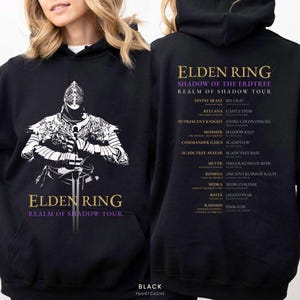 May include: Black hoodie featuring a detailed white and black graphic of a knight holding a sword, with the text "ELDEN RING REALM OF SHADOW TOUR." The back of the hoodie lists tour locations. The word "BLACK" is printed at the bottom.