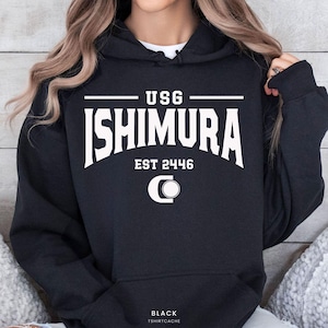 May include: A black hooded sweatshirt featuring white screen-printed text that reads USG ISHIMURA EST 2446 above a circular logo. The garment includes a front kangaroo pocket, long sleeves, and a drawstring hood, with the word BLACK printed at the bottom.