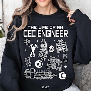 May include: Black sweatshirt with the text "THE LIFE OF AN CEC ENGINEER" in white. The sweatshirt features various white graphic illustrations, including a figure, tools, and geometric shapes. The text "BLACK TSHIRTCACHE" is at the bottom.