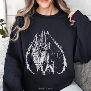 May include: Black sweatshirt featuring a white graphic design of a dragon or mythical creature. The design is centered on the front of the sweatshirt. The text "TSHIRTCACHE" is printed at the bottom of the sweatshirt.