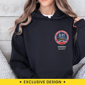 May include: A black hooded sweatshirt featuring a circular graphic on the left chest. The emblem displays a spaceship over a red planet with the text PLANET CRACKER STARSHIP ISHIMURA, the Japanese characters 石村, and the words HANNAH SECURITY below.