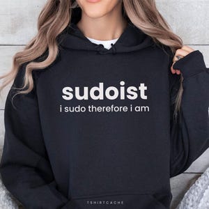May include: Black hoodie featuring the word "sudoist" in white, with the phrase "i sudo therefore i am" underneath. The brand name "TSHIRTCACHE" is printed at the bottom. The hoodie has a drawstring hood.
