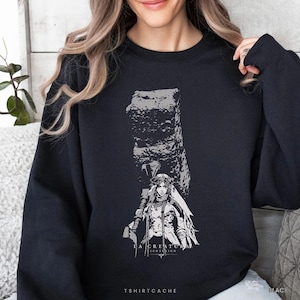 May include: A black crewneck sweatshirt featuring a white graphic print of a figure standing before a large, textured stone pillar. The design includes the text "LA CREATURA" and "NIGHTREIGN" printed in a clean, sans-serif font below the illustration.