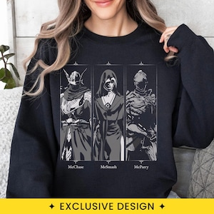 May include: A black long-sleeve sweatshirt featuring a graphic print of three stylized figures in separate vertical panels. Below each figure, the text reads MeChase, MeSmash, and MeParry in a white font. The design is centered on the chest.