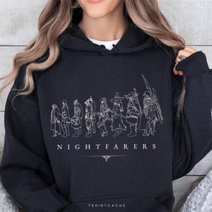May include: Black hooded sweatshirt with a white line drawing of figures and the word "NIGHTFARERS" in white. The sweatshirt also has the text "TSHIRTCACHE" at the bottom.
