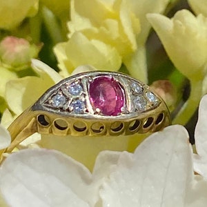 May include: A gold ring with a pink oval gemstone surrounded by smaller diamonds. The ring is set against a background of white flowers.