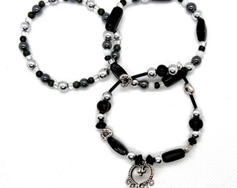 May include: Three black and silver beaded bracelets with a heart charm on one of the bracelets.