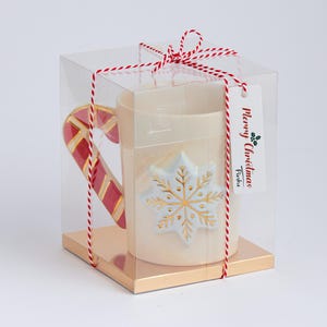 Puede incluir: Una taza de cer&aacute;mica blanca con un asa de bast&oacute;n de caramelo y un dise&ntilde;o de copo de nieve dorado. La taza est&aacute; empaquetada en una caja de pl&aacute;stico transparente con un lazo de cuerda rojo y blanco y una etiqueta de regalo que dice "Feliz Navidad" con una peque&ntilde;a rama de acebo verde.