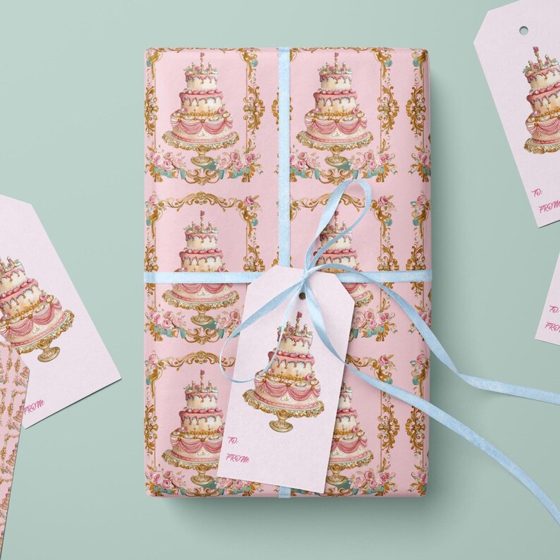 May include: Pink gift wrap with a repeating pattern of gold ornate frames and a white cake with pink frosting. A blue ribbon is tied around the gift box with a pink gift tag that says "To" and "From".