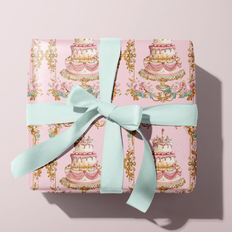 May include: A pink gift box with a light blue ribbon. The box is wrapped in paper with a repeating pattern of ornate gold frames and watercolor illustrations of wedding cakes with pink and white frosting.