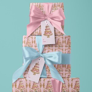 May include: Three pink gift boxes with a cake pattern and gold accents. The boxes are stacked on top of each other. The top box has a pink ribbon and a gift tag with a cake illustration. The middle box has a blue ribbon and a gift tag with a cake illustration. The bottom box has a pink ribbon.