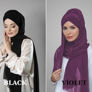 May include: Two women wearing headscarves, one black and one purple, with a simple white shirt underneath. The headscarves are styled with a knot on top.