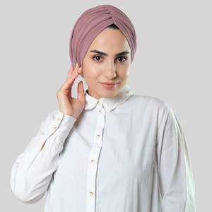 Puede incluir: Una mujer con un turbante malva y una camisa blanca abotonada.