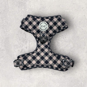 May include: A black and pink plaid dog harness with a silver buckle and a circular logo that says "C&C" in the centre.