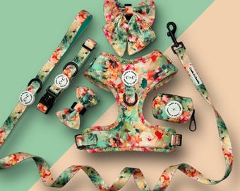 Puede incluir: Un conjunto de accesorios para perros con un estampado floral en tonos verdes, naranjas y rosas. El conjunto incluye un arnés, una correa, un collar, una pajarita y un dispensador de bolsas de residuos. Cada artículo tiene un diseño a juego con el logotipo de la marca.