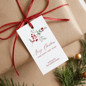 May include: A white rectangular gift tag featuring a watercolor illustration of red berries and green leaves. The text reads Merry Christmas AND HAPPY NEW YEAR! WITH LOVE, THE SAMPLE FAMILY in red script and block lettering, tied with red twine.