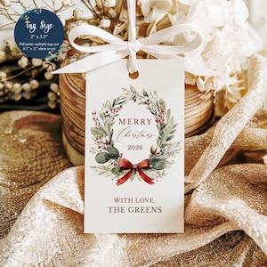 May include: A rectangular white gift tag measuring 2 inches by 3.5 inches, featuring a watercolor wreath of green leaves, red berries, and cotton bolls. The text reads Merry Christmas 2026 and With Love, The Greens, tied with a white ribbon.