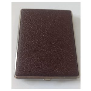 Op de afbeelding: Een rechthoekige, bruine leren sigarettenetui met een textuuroppervlak en een zilverkleurig metalen frame. De etui is gesloten en heeft een kleine sluiting aan de onderkant.