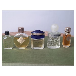 Peut inclure: Une collection de cinq flacons de parfum miniatures. Les flacons, de formes et tailles variées, contiennent des liquides de couleurs différentes et des bouchons distincts. Les étiquettes indiquent "Monsieur de Givenchy", "Eau de roche", et "Boucheron Paris".