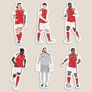 May include: A set of six die-cut stickers featuring football players in red and white kits. Five players wear red shirts with white shorts and socks, while one goalkeeper wears a grey jersey with patterned shorts. Each figure is depicted in a standing pose.