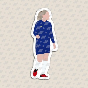May include: A die-cut sticker featuring a stylized illustration of a soccer player with a ponytail, wearing a long-sleeve blue jersey with a light blue geometric pattern, white shorts, white socks, and red soccer cleats with a yellow Nike logo.