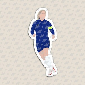 May include: A die-cut sticker featuring a stylized illustration of a soccer player in a dark blue jersey with a light blue geometric pattern, a yellow logo, a lime green captain's armband, white shorts, and white socks with red accents.