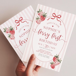 Op de afbeelding: Twee rechthoekige verjaardagsuitnodigingen met een lichtroze en witte verticaal gestreepte achtergrond. De kaarten tonen rode aquarel aardbeien, een rode strik en de tekst: JOIN US FOR SOPHIE'S ferry first BIRTHDAY SUN 26 NOV.