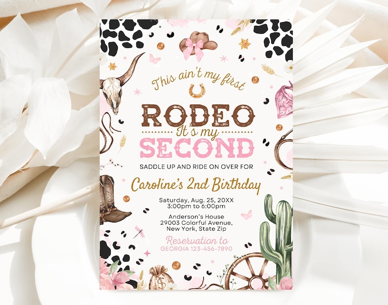May include: A pink and brown invitation for a second birthday party with a rodeo theme. The invitation features a cow skull, a horseshoe, a cactus, and a wagon wheel. The text on the invitation reads "This ain't my first Rodeo - It's my Second" and "Caroline's 2nd Birthday".