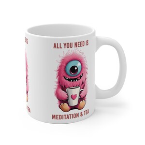 Könnte beinhalten: Weiße Keramiktasse mit einem rosa, flauschigen Monster, das eine Tasse Tee hält. Auf der Tasse steht der Text "All you need is meditation & tea".
