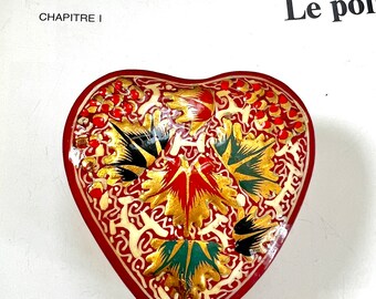 May include: A red heart-shaped trinket box with a gold and black floral design. The box is decorated with intricate patterns and red accents.