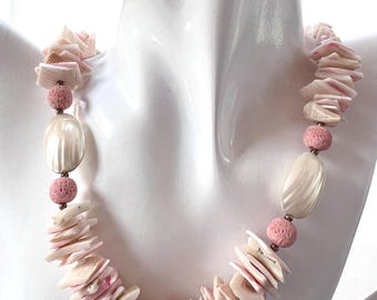 May include: A necklace featuring a combination of natural elements. The necklace includes shell fragments in shades of white and pink, interspersed with pink spherical beads and oval, pearlescent beads. The necklace is displayed on a white mannequin.