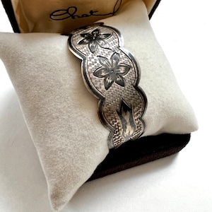 May include: A silver bracelet with a floral design. The bracelet is in a velvet box with the word "Chatel" written on the inside.
